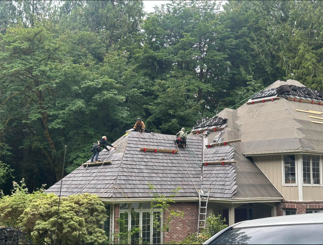 Roofers working on a house roof. Green trees in background. Cloudy sky.