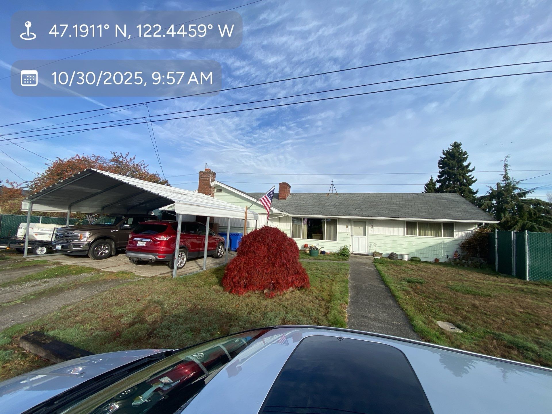 A house with a carport, cars parked, and a red bush on a sunny day.