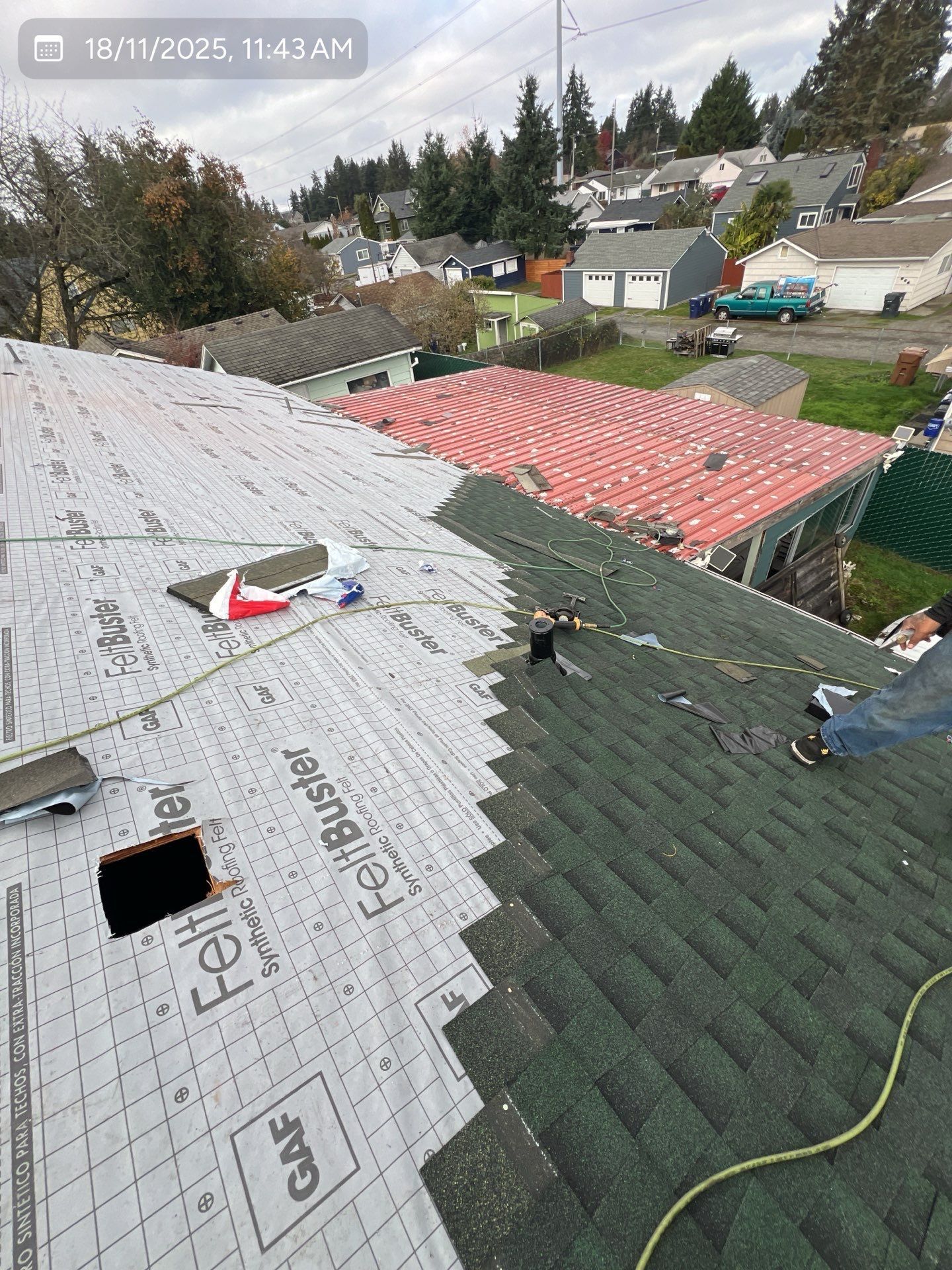 Roofers installing shingles on a house roof. Green and gray shingles, tarpaper. Overcast day.