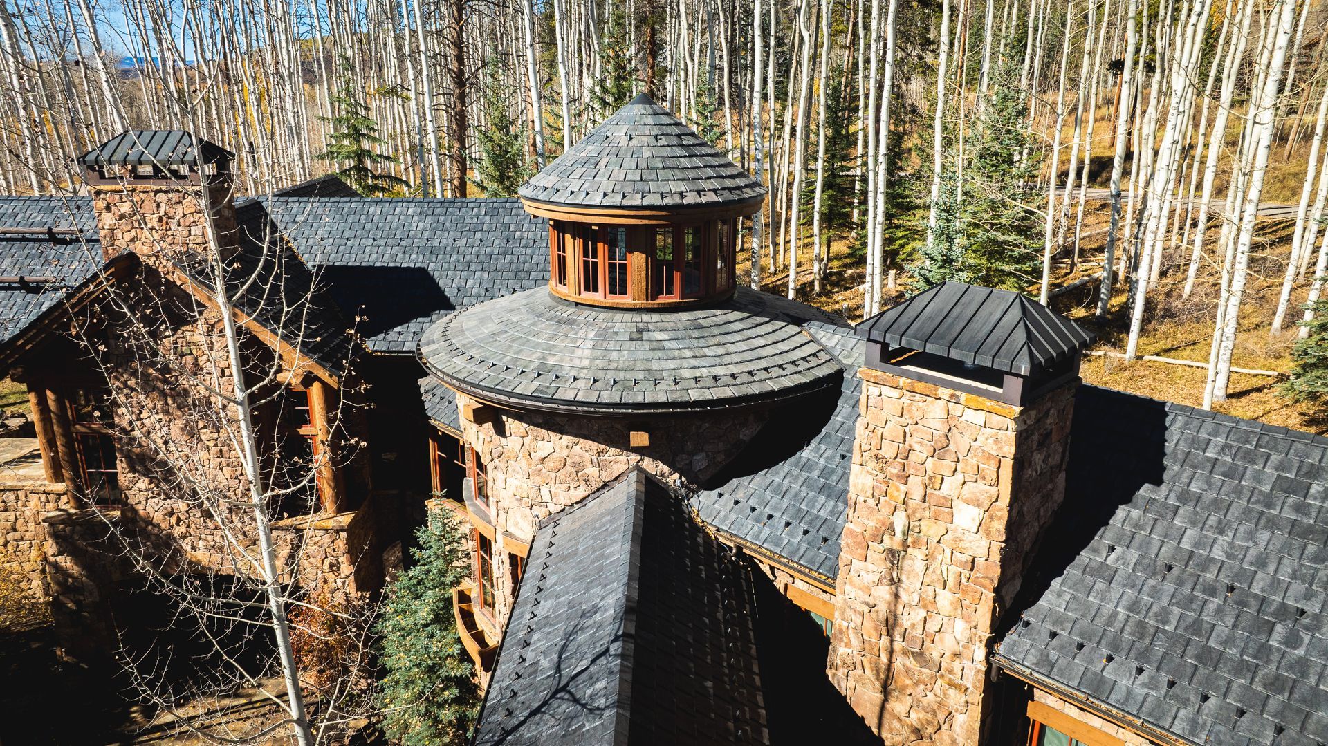 Stone-clad mountain home with slate roof and a central domed section surrounded by fall foliage.