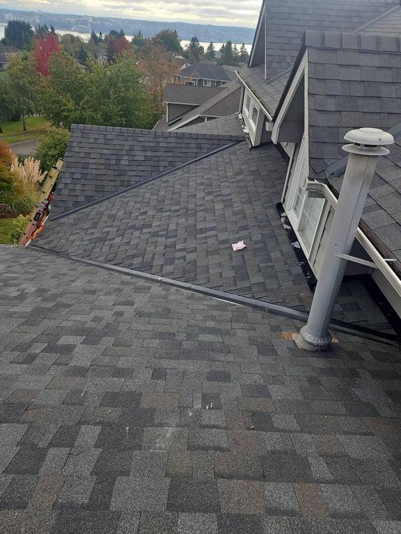 GAF Dark gray asphalt shingle roof on a house with a vent pipe; view of neighborhood in the background.