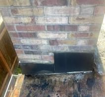 Brick chimney base with black metal flashing; close-up.