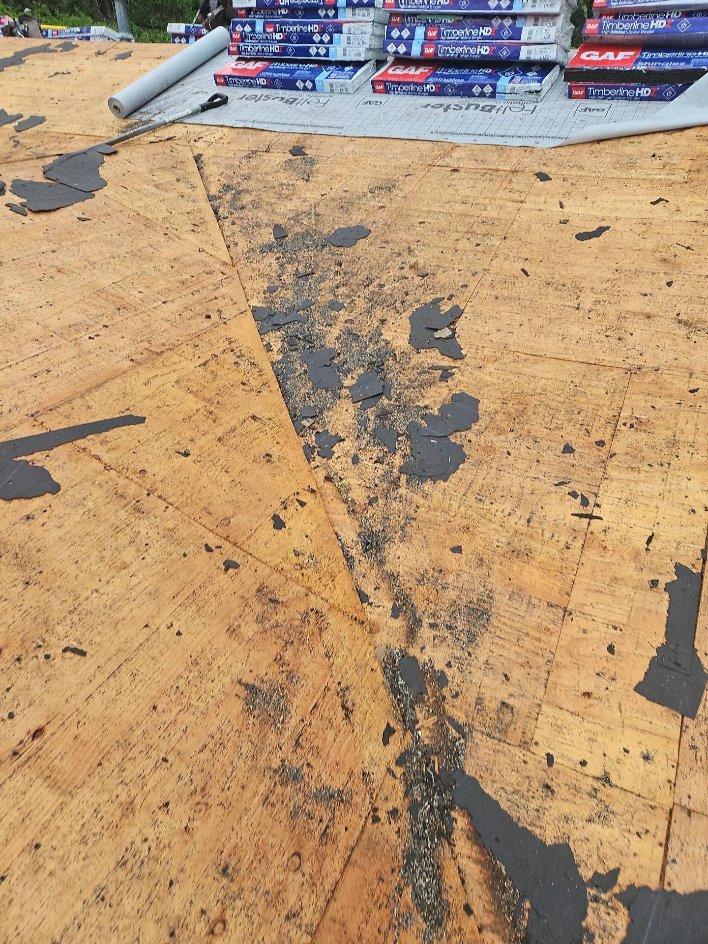 Roof with areas of peeled-off dark material. New roofing materials are stacked nearby by Team Roofing NW in Lakewood, WA.