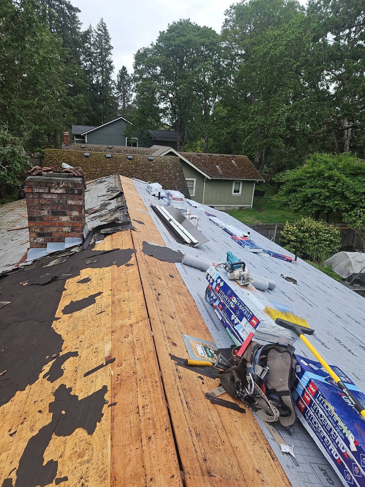 Roof being repaired; wood boards and metal roofing visible, along with tools and materials by Team Roofing NW in Lakewood WA.