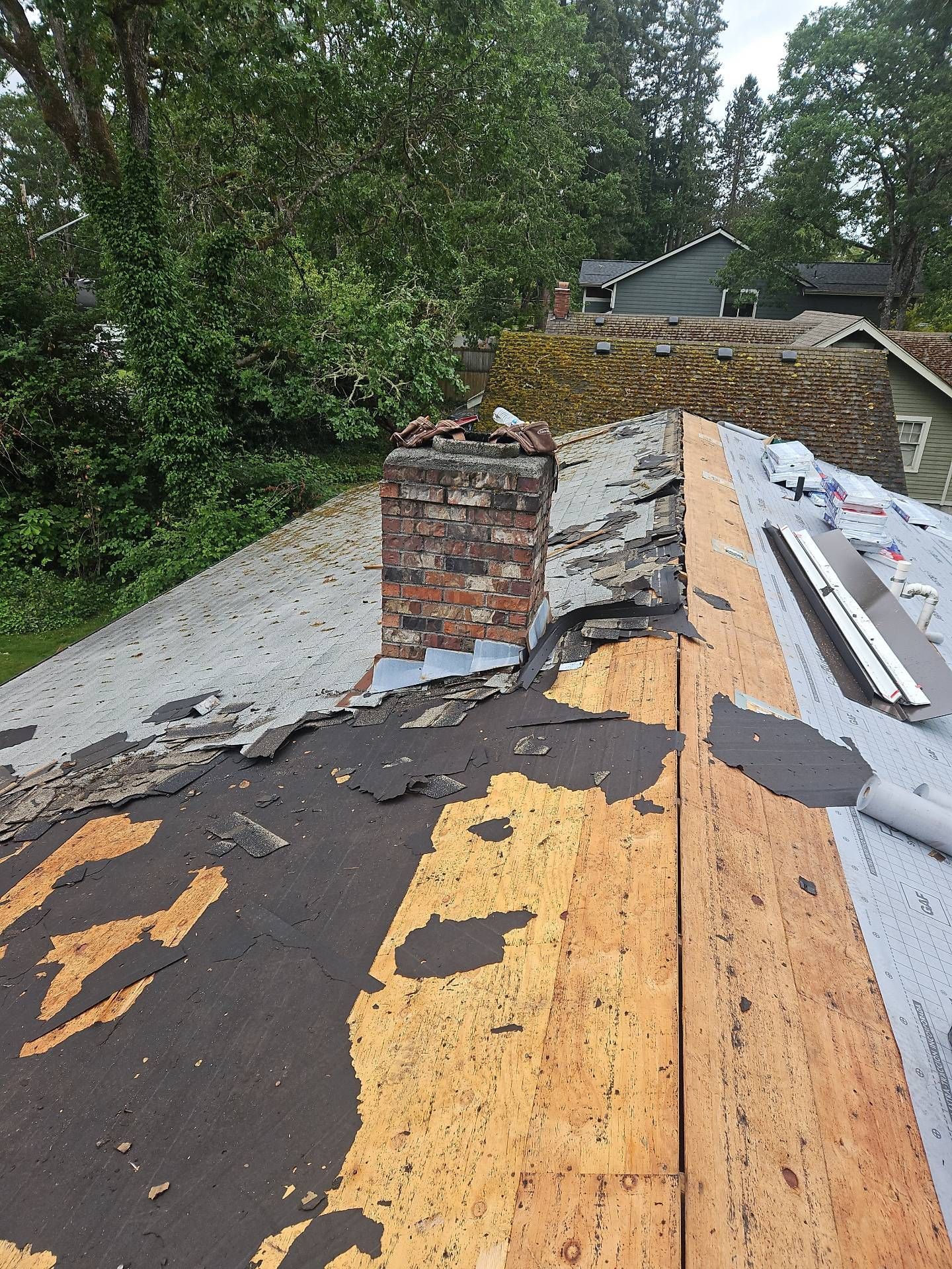 Roof with a brick chimney and damaged shingles; partially torn off and exposing wood by Team Roofing NW in Lakewood, WA.