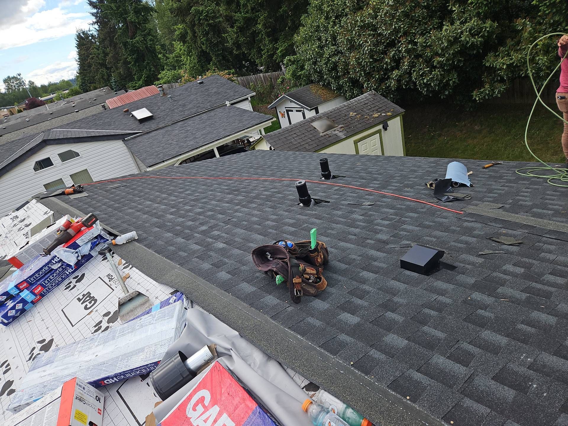 Roof with various tools and materials; other houses in the background.