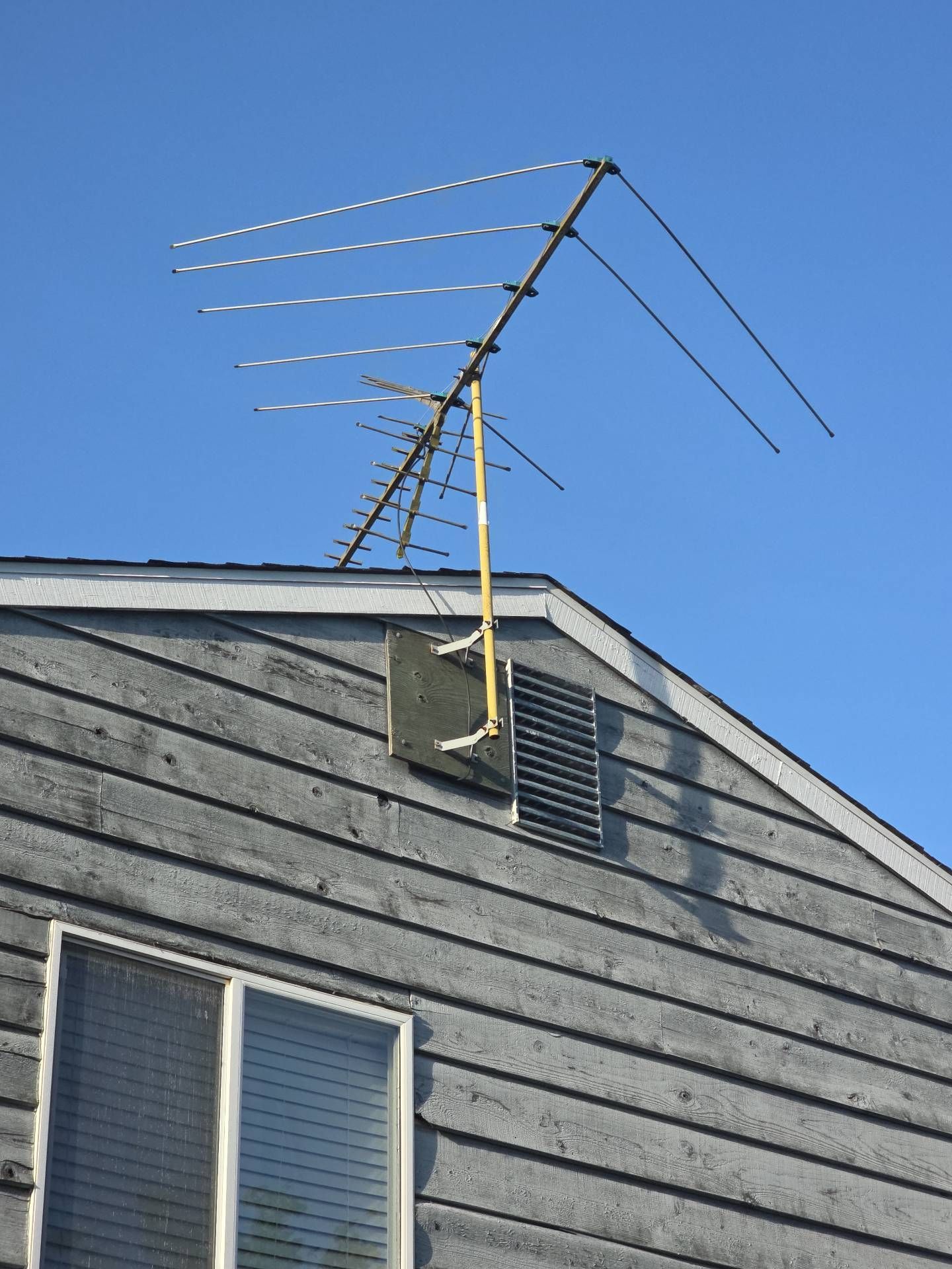A TV antenna mounted on a weathered gray house, against a clear blue sky.