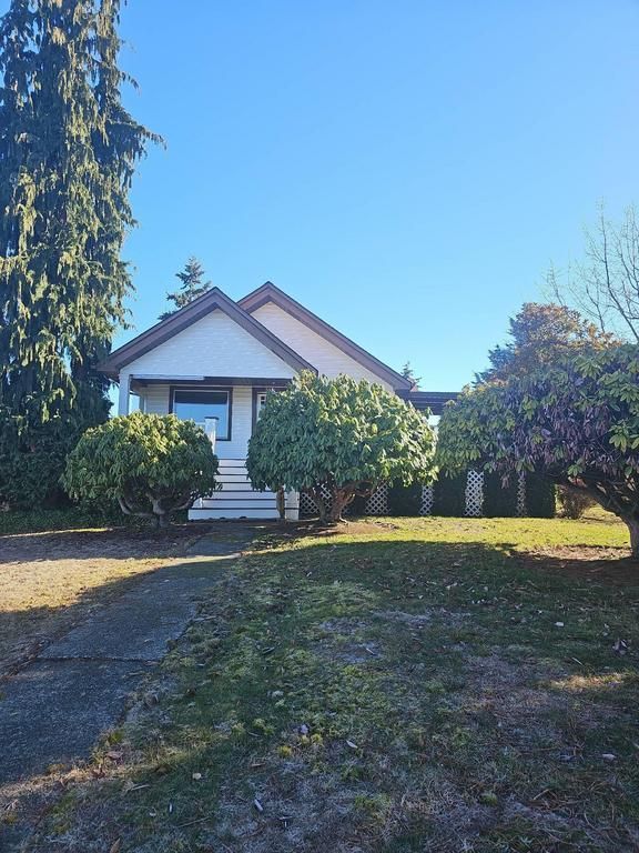 Small house with white siding, surrounded by shrubs, on a sunny day.
