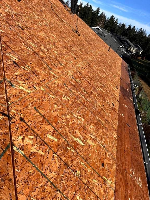 View of a new OSB roof with a brown composite material, ready for shingling. Sunny day, exterior.