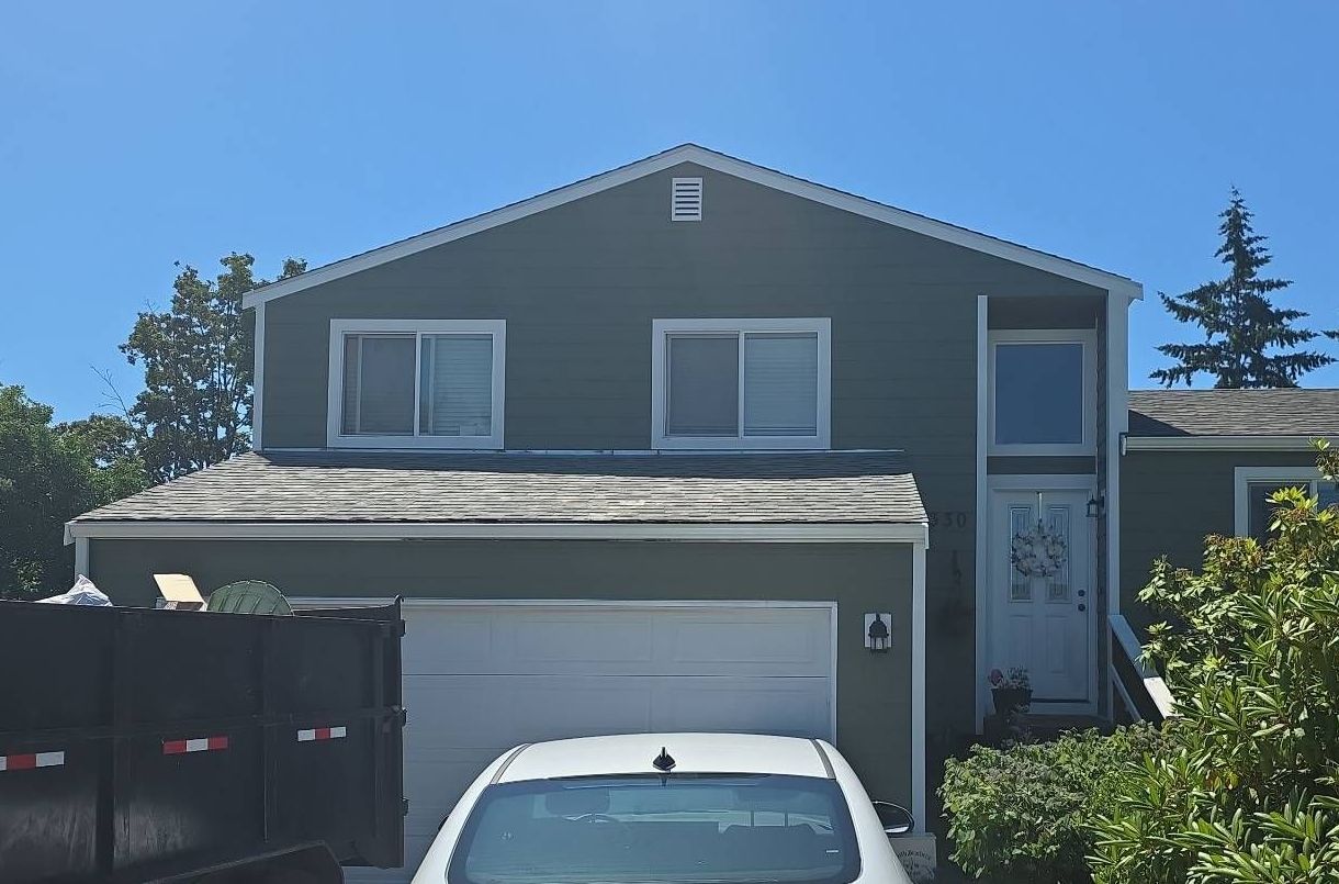 Green house with white trim, gray roof, white garage door, and a white car in front.