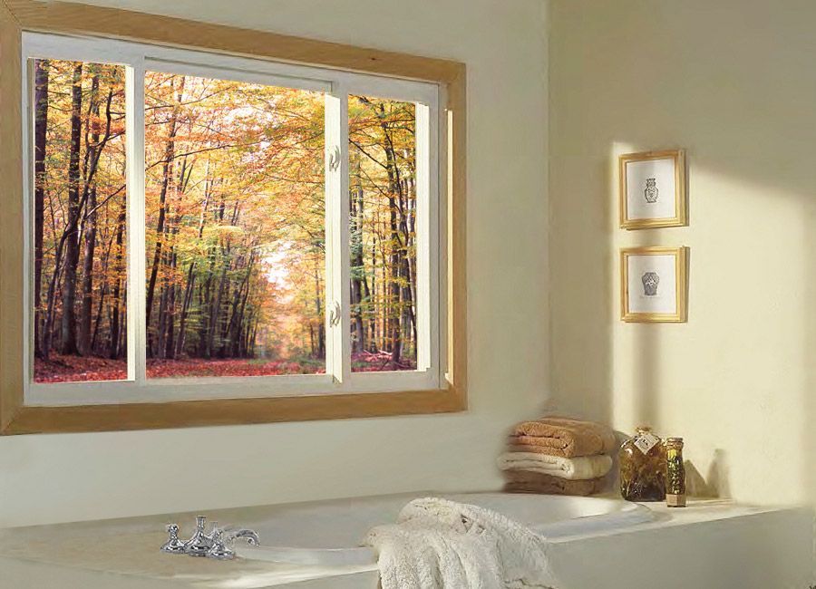 Sunny bathroom with a window view of autumn trees, a bathtub, and framed wall art