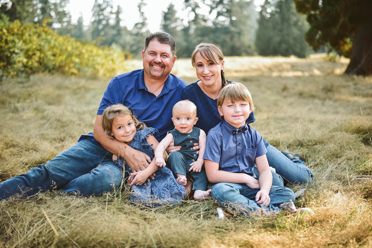 Family of five sitting in grassy field; smiling, sunny.