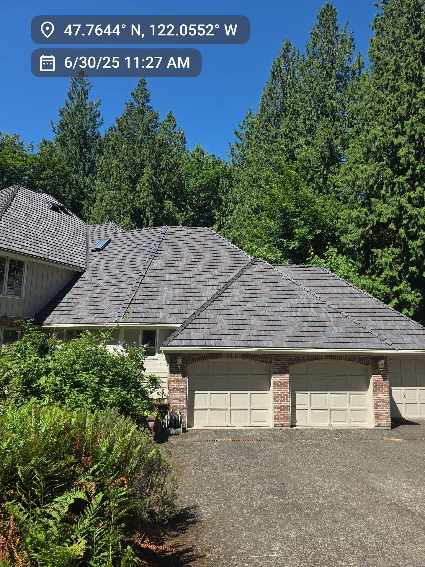 House with gray roof and brick accents, surrounded by trees. Date and location overlay.