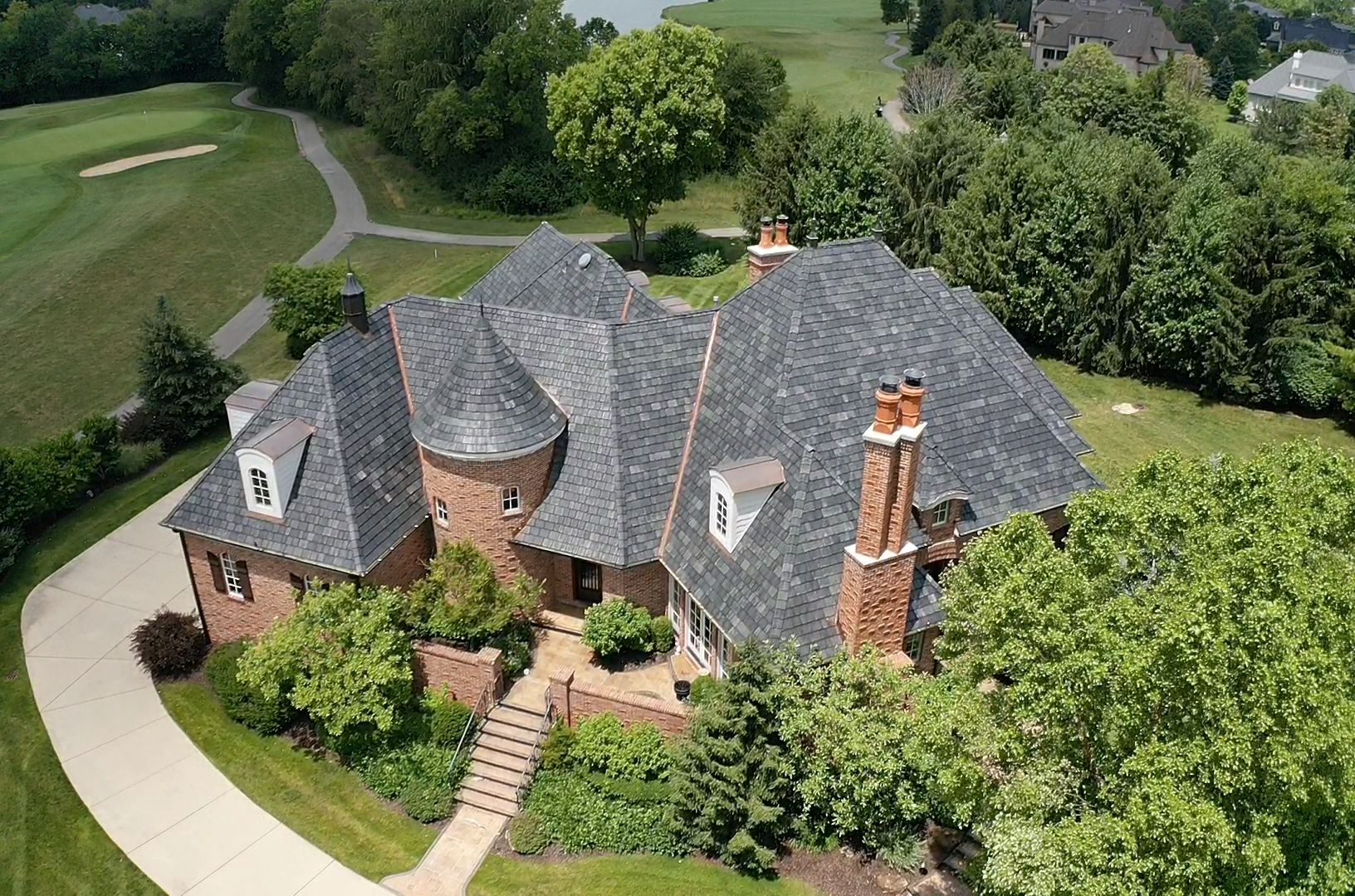 Large brick house with slate roof, chimney, and circular driveway, next to a golf course.