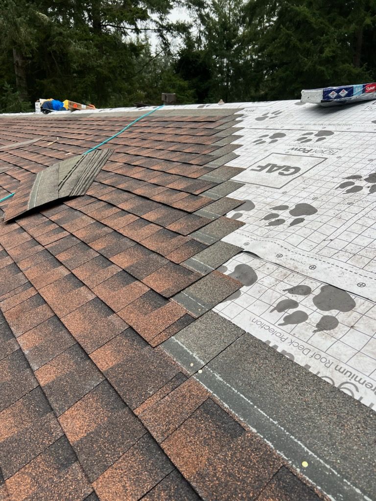 Roof partially covered with brown shingles, new underlayment visible, outdoor setting.