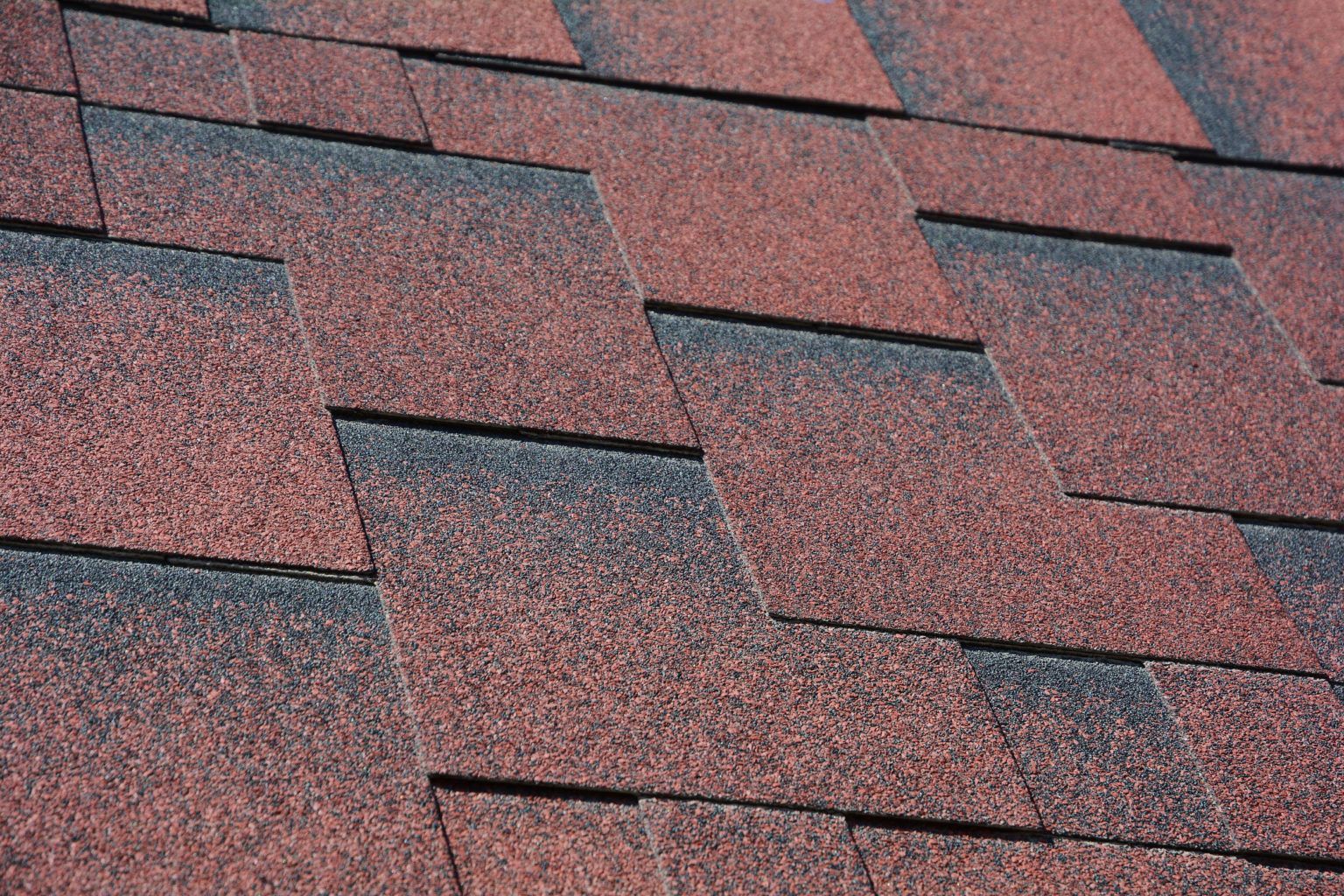 Red and black asphalt roof shingles on a sloped roof.