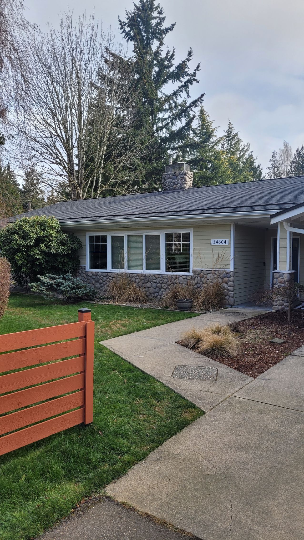 Ranch-style house with stone accents, a gray roof, and a wood fence in front.