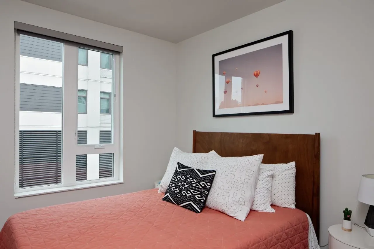 Modern bedroom with a queen-size bed, artwork, and large window.