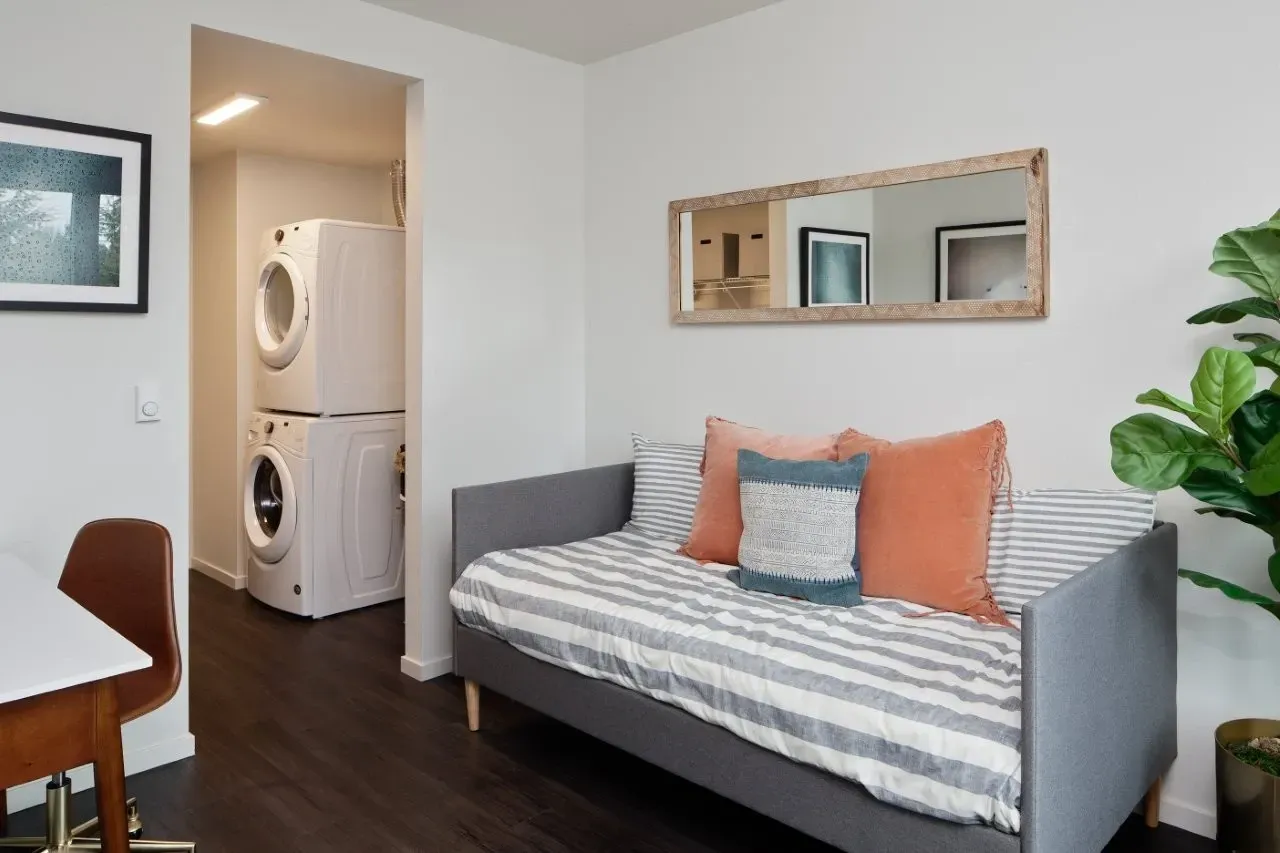 Stylish living room with a daybed, stacked washer and dryer, and a desk.