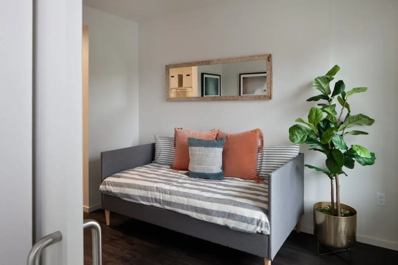 A gray daybed with striped bedding, coral and teal pillows, and a large potted plant.
