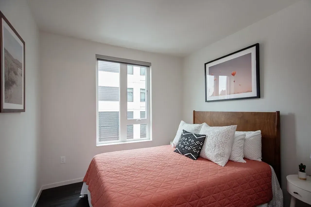 Modern bedroom with a queen-size bed, artwork, and large window.