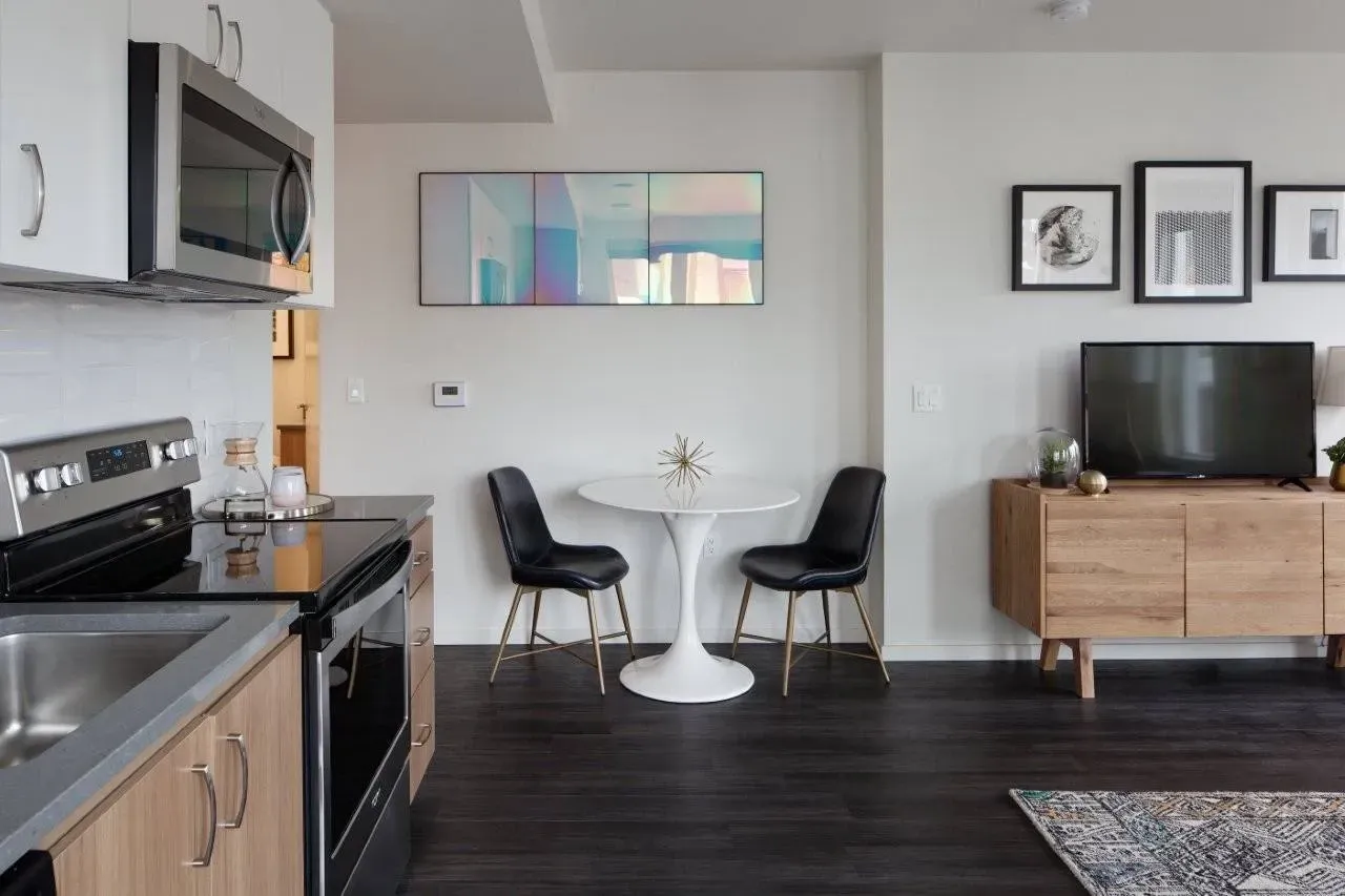 Modern kitchen and dining area with sleek appliances, a tulip table with chairs, and a TV console.