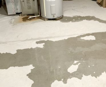 Water on a concrete basement floor near a water heater and appliance, with a darker stain.