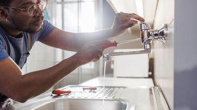 Person using a wrench to repair a silver faucet in a kitchen.