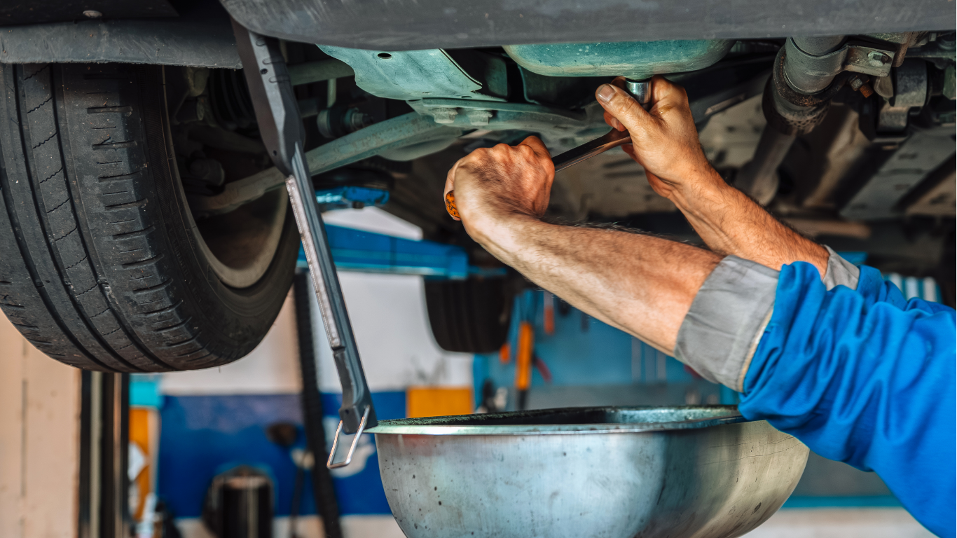 Mechanic working under a car during an oil change, with a drain pan below.