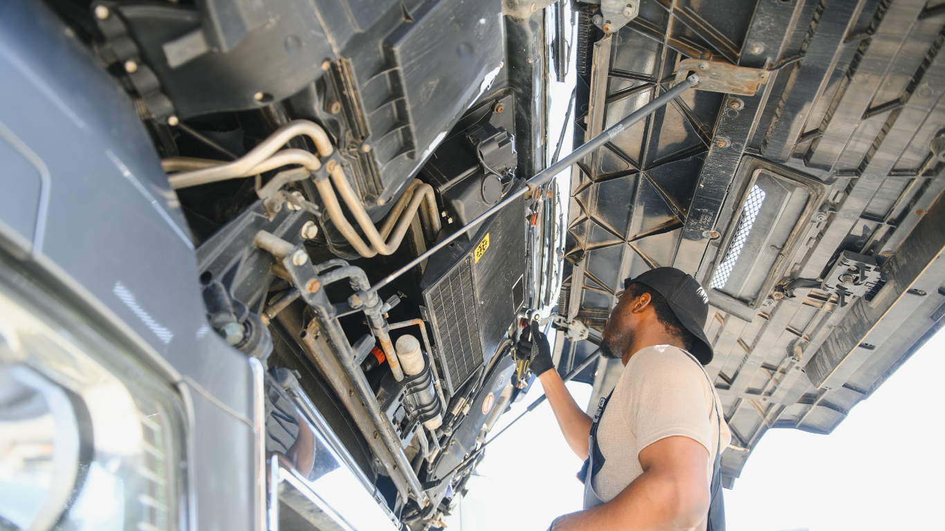 Man working under an aircraft fuselage, inspecting exposed wiring and mechanical components