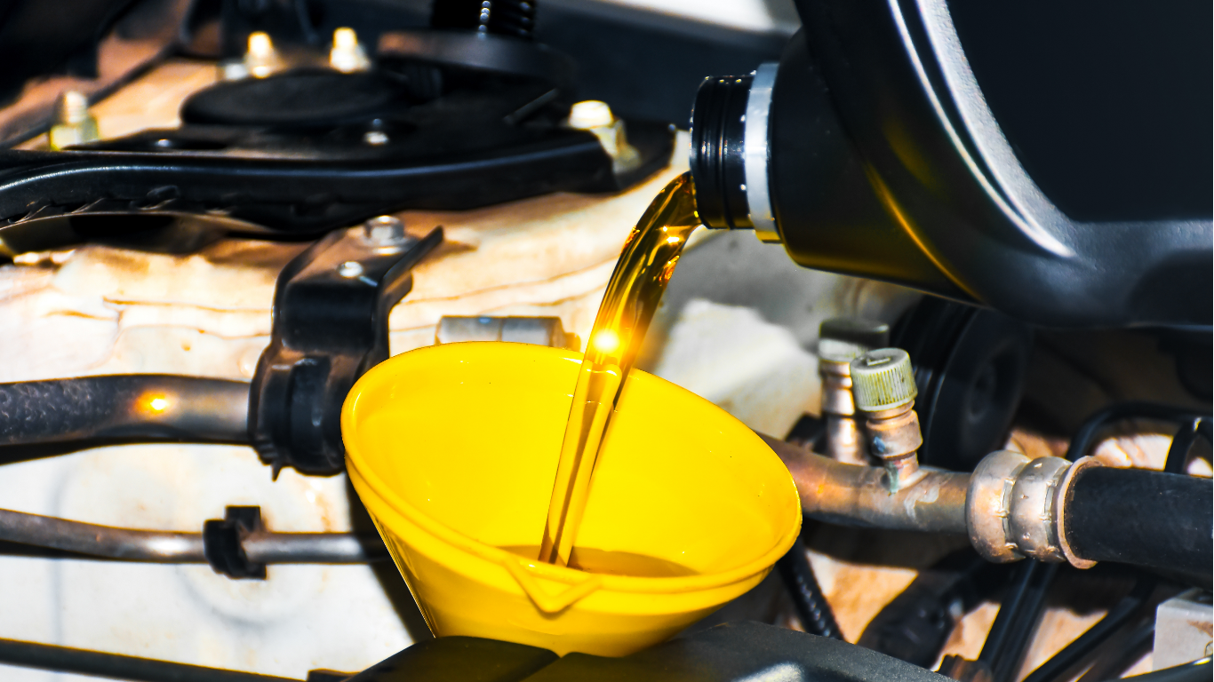 Motor oil pouring from a black container into a yellow funnel in an engine bay