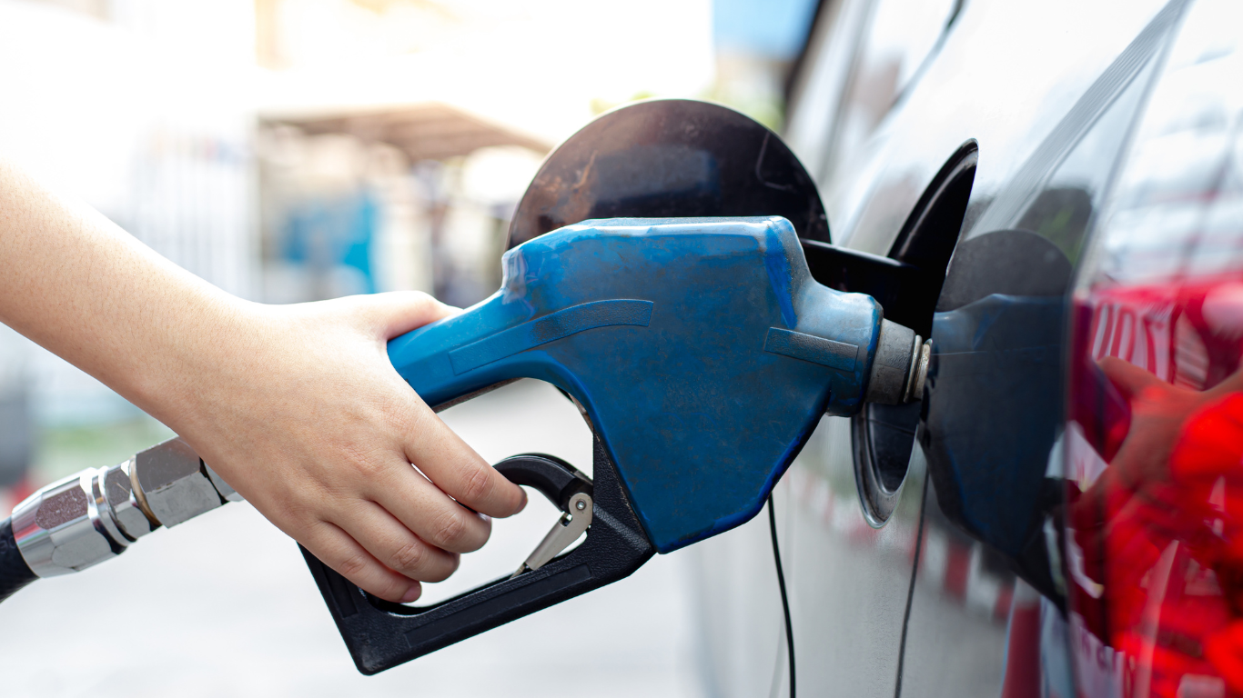 Person refueling a white car with a blue gas pump at a gas station
