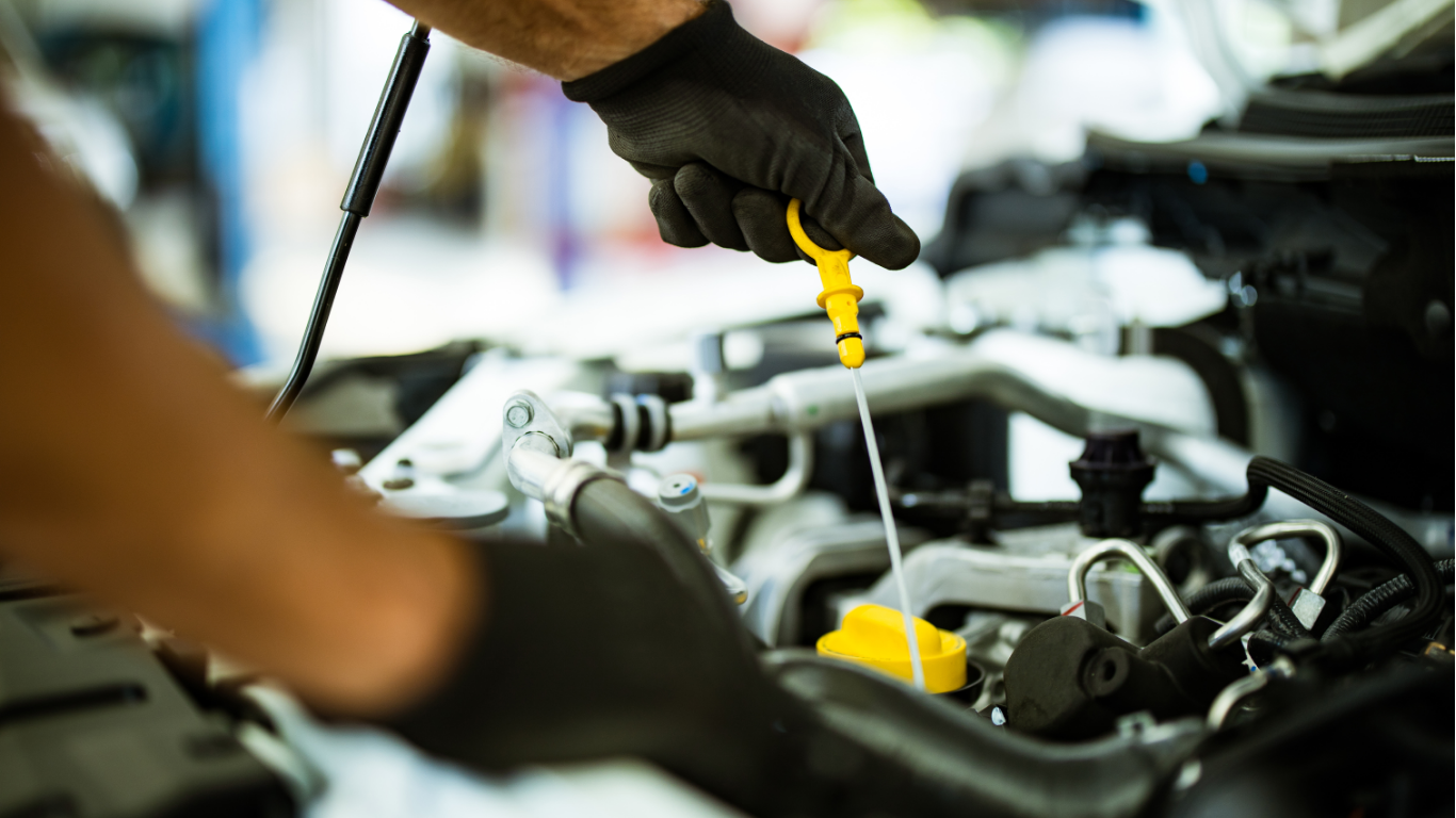 Mechanic using a yellow dipstick to inspect an open car engine bay