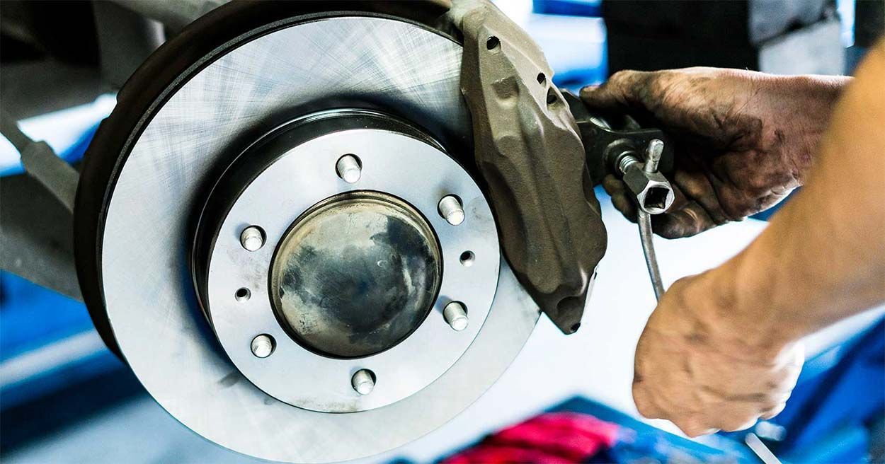 Mechanic repairing a car brake disc with a wrench, close-up of wheel assembly and hands