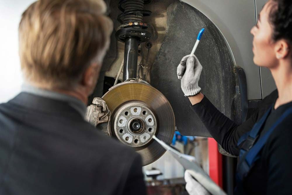 Two workers in gloves inspecting a large metal industrial machine with a brush.