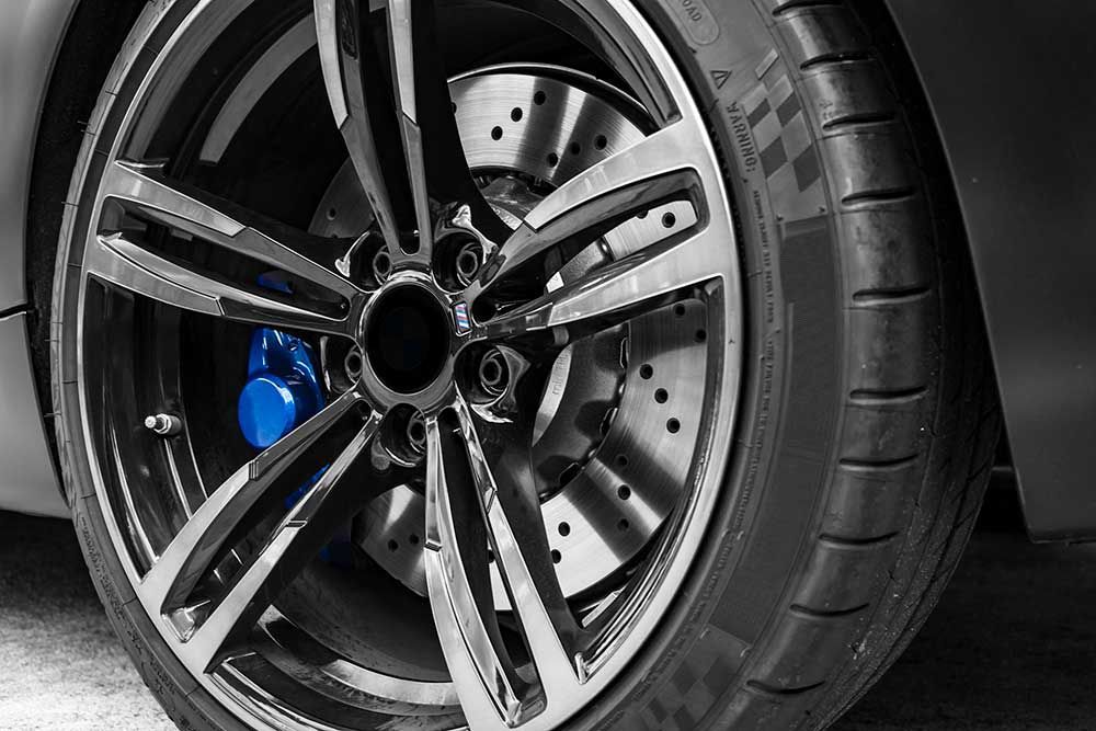 Close-up of a black and silver alloy car wheel with a blue brake caliper and drilled brake rotor