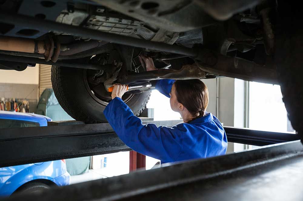 Mechanic in blue coveralls working under a lifted car in a garage
