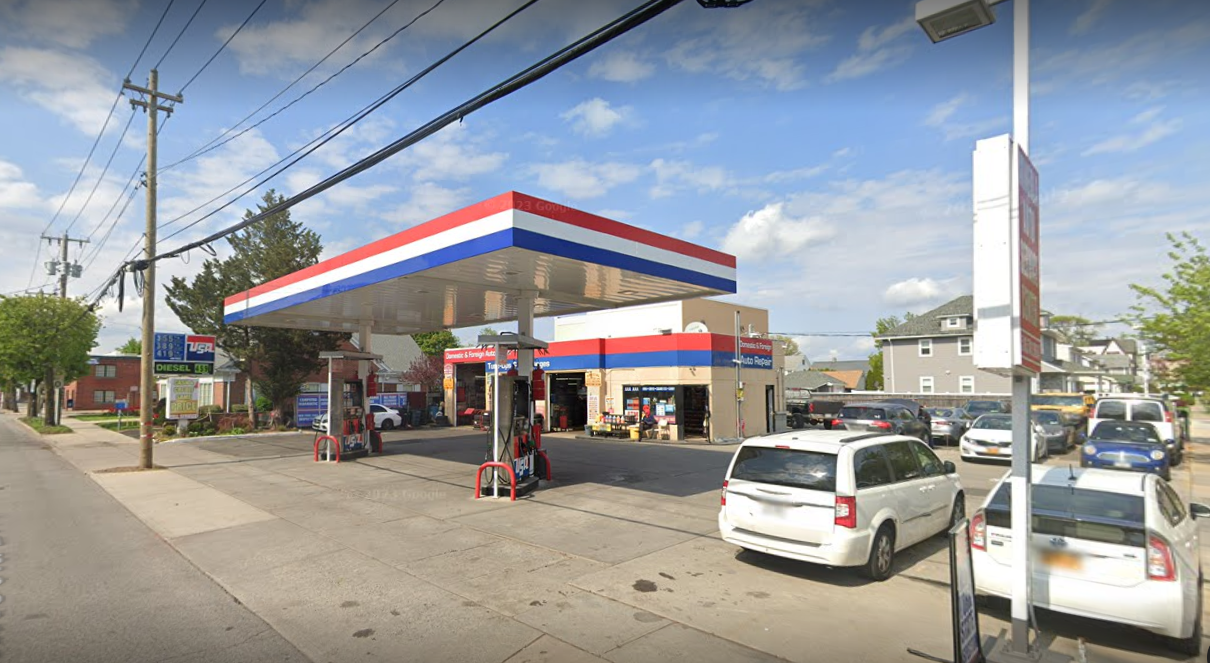 Gas station with red, white, and blue canopy; cars parked beside the pumps on a sunny street.