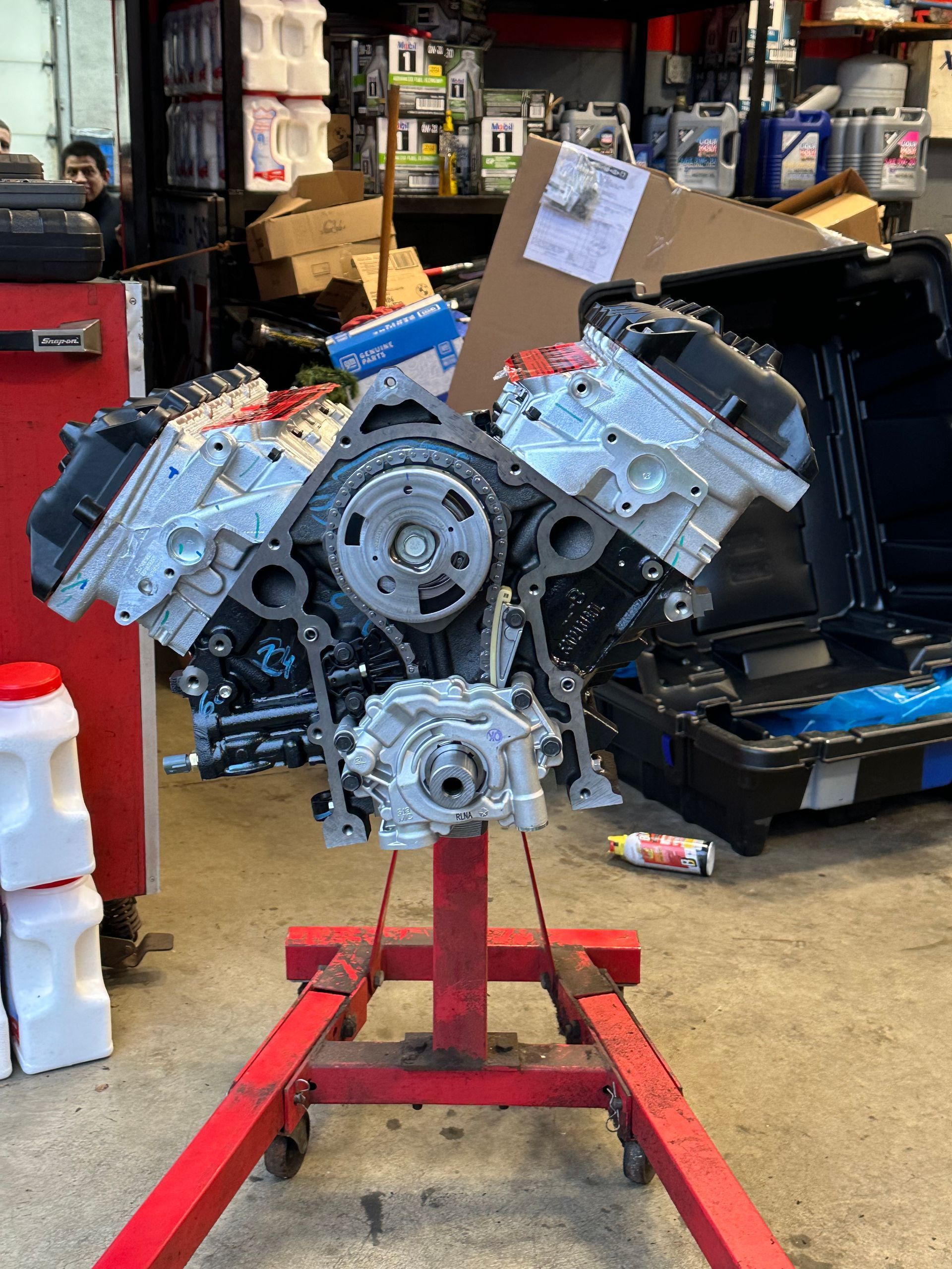 Engine mounted on red stand in auto shop with parts and tools in the background
