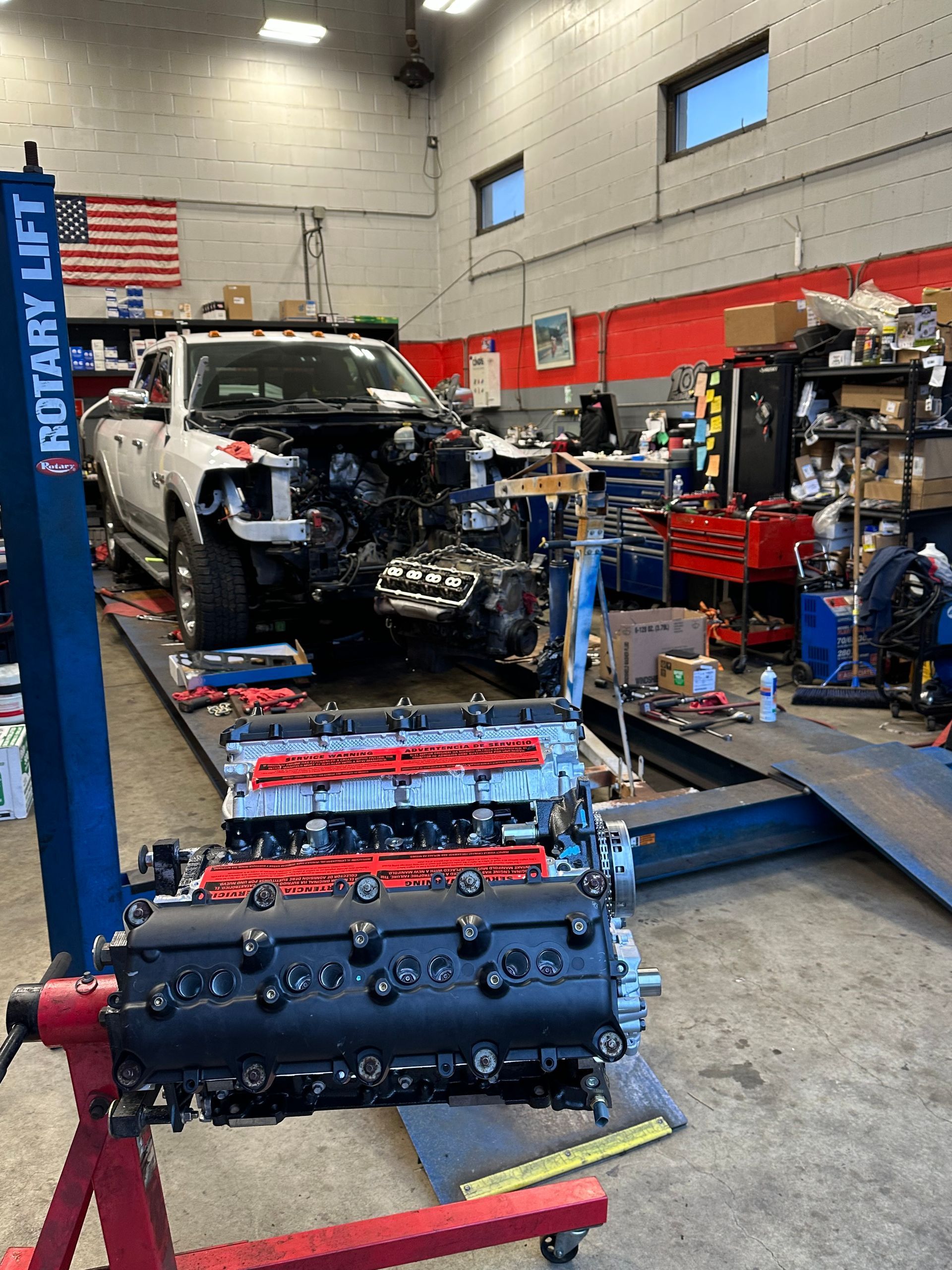 Auto repair shop with a partially disassembled car and engine parts on blue workbenches and a lift