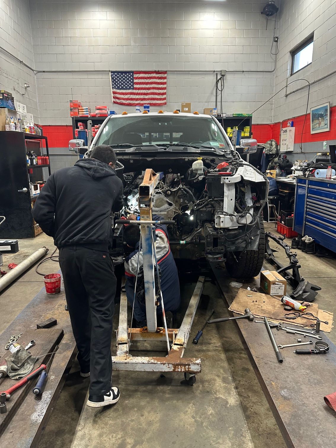 Mechanic working on a stripped car in an auto repair shop with tools and an American flag on the wall