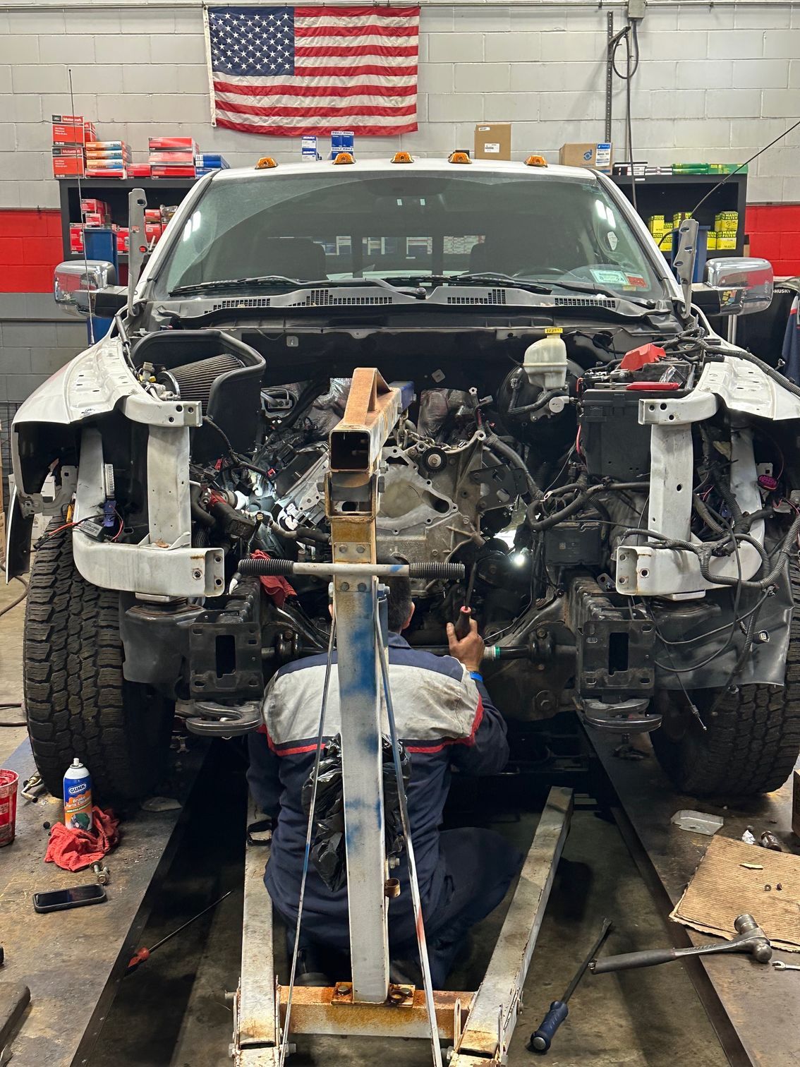 Mechanic working on a dismantled SUV in an auto repair shop, with a U.S. flag in the background