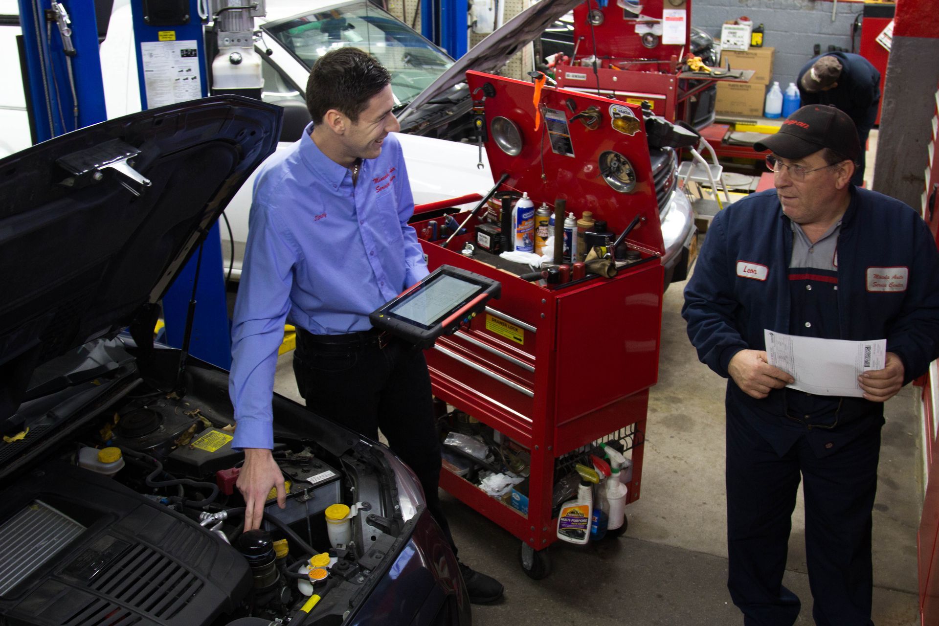 Two technicians inspect a machine with a flashlight and brush in an industrial setting
