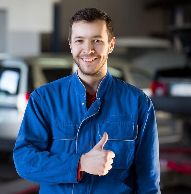 Smiling mechanic in blue coveralls giving a thumbs-up in a garage