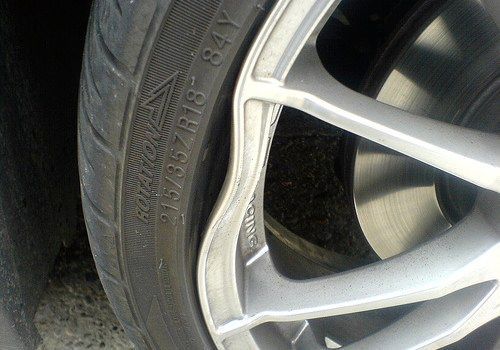 Close-up of a car wheel with a silver alloy rim and worn tire showing sidewall damage.
