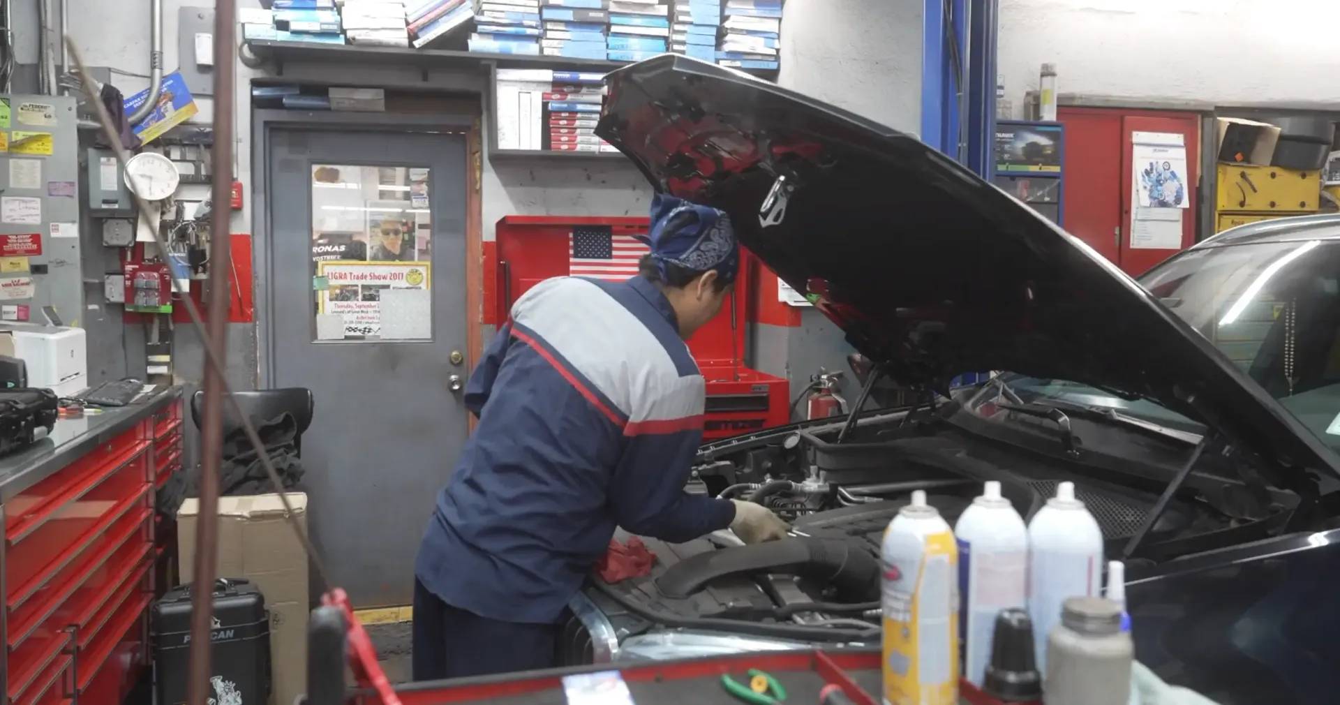 Mechanic working under open car hood in an auto repair shop with tools and supplies nearby