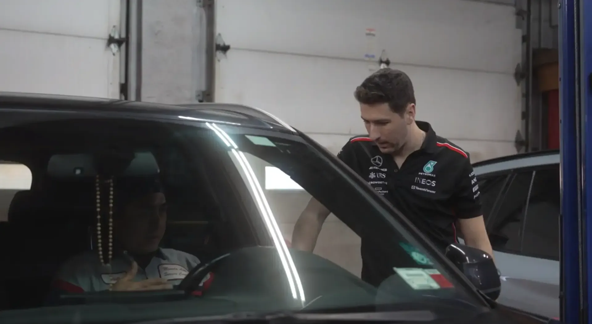 Mechanic leaning into a car window, speaking with the driver inside a garage.