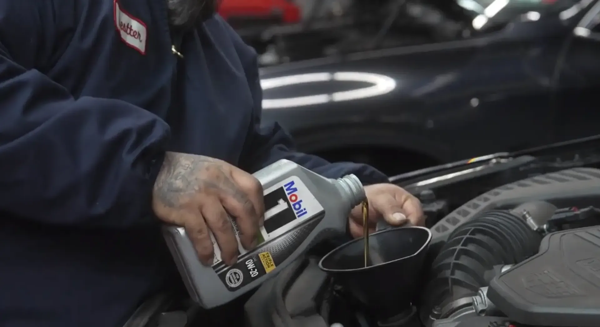 Mechanic pouring fluid from a bottle into a car engine bay during maintenance