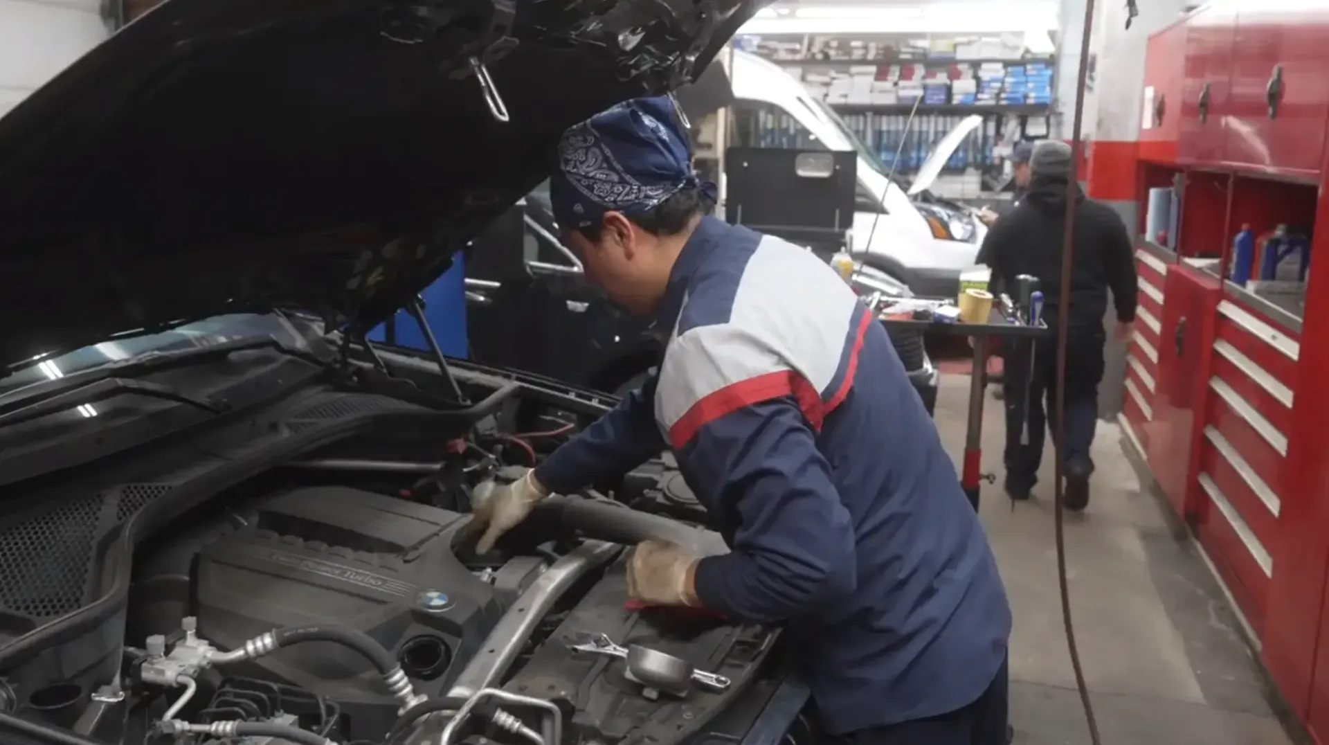 Mechanic working under an open car hood in an auto repair garage