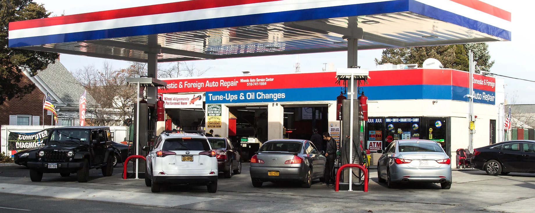 Cars at a Shell gas station under a red, white, and blue canopy during rainy weather